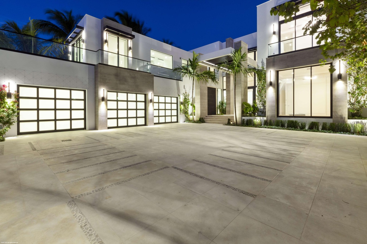 Night arrival view across the main driveway and illuminated garage doors.